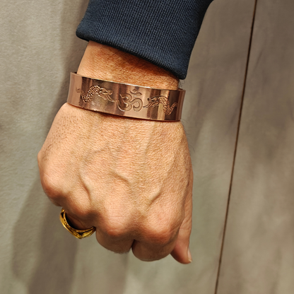Hand wearing a copper bracelet with intricate designs on a neutral background

